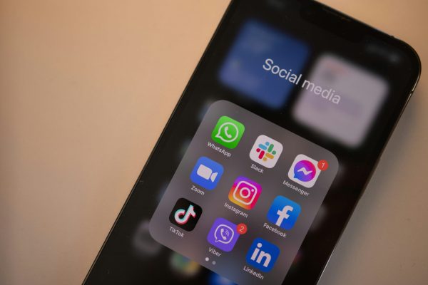 智慧型手機螢幕上顯示多個社群媒體應用程式圖示，如 Facebook、Instagram、TikTok、LinkedIn 等，象徵數位行銷與社群行銷的重要性。